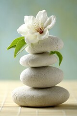 Fototapeta premium Zen stones stacked with white flower and green leaves on bamboo mat in studio shot for meditation and wellness concept
