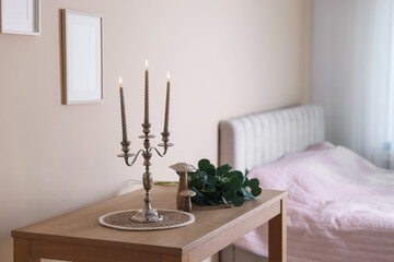 Stylish candlestick with burning candles and other decor on wooden table near beige wall indoors