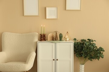 Stylish candlesticks with burning candles and other decor on cabinet near beige wall indoors