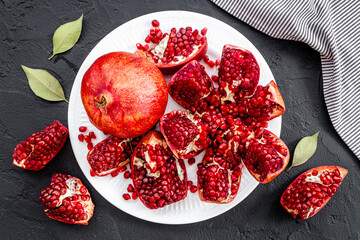 Plate full of fresh ripe pomegranate with cut in half and pieces, top view.