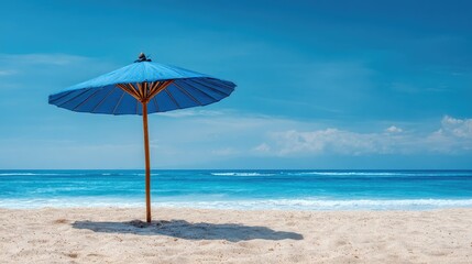 Blue umbrella on a sandy beach with clear sky and ocean in the background, representing vacation and relaxation