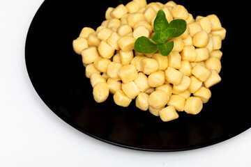 Pile of fresh raw gnocchi with basil leaves, view from above on a black dish