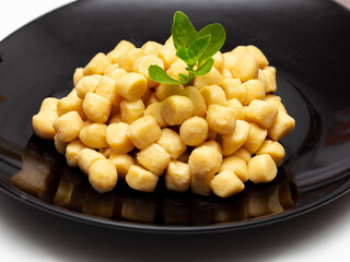 Pile of fresh raw gnocchi with basil leaves, view from above on a black dish