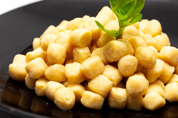 Pile of fresh raw gnocchi with basil leaves, view from above on a black dish