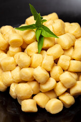 Pile of fresh raw gnocchi with basil leaves, view from above on a black dish
