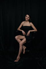 Naklejka premium A slim, beautiful Caucasian woman in a black dress, brunette, against a black background, with glowing skin and a smile