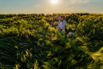 Fototapeta premium Concerned farmer checks his damaged barley field at sunset, touching his head in frustration over the fallen crop, likely due to heavy rain or strong winds