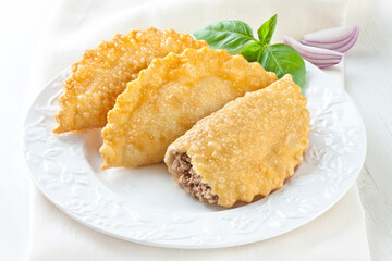 Fried chebureks with meat on a white plate on a white background. Uzbek Tatar cuisine.