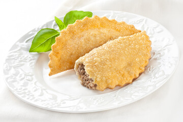 Fried chebureks with meat on a white plate on a white background. Uzbek Tatar cuisine.