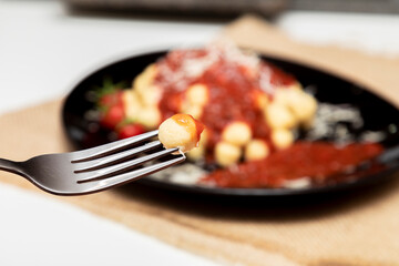 Close up on fork with gnocchi and plate of gnocchi with blurred red sauce in the background