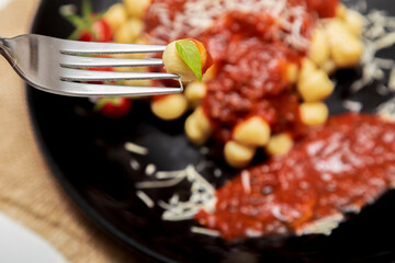 Close up on fork with gnocchi and plate of gnocchi with blurred red sauce in the background