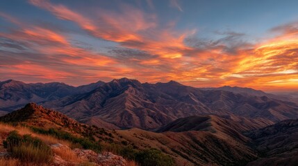 Wide view of a mountain range during sunrise, with deep orange and red colors lighting up the clouds and sky above
