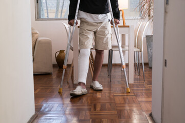 Man walking on crutches at home after leg injury