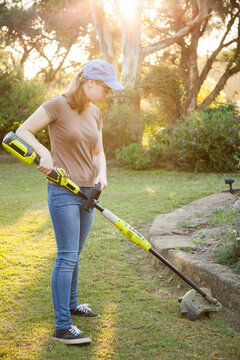 Teen girl cutting grass with whipper snipper in golden afternoon light