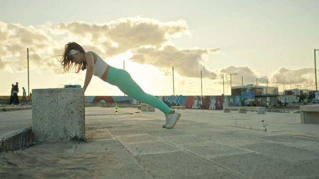 Determined sportswoman doing incline push ups outdoors at sunset