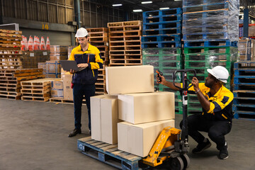 Warehouse technician kneels beside pallet to scan boxes with handheld scanner, checking barcodes...