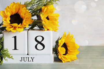World Music Day. White wood calendar blocks with the date July 18th and beautiful sunflower bouquet with bokeh. Selective focus with blurred background. 