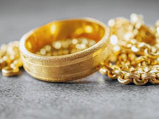 Gold price, gold jewelry, close-up of gold ring and gold necklace on grey background.