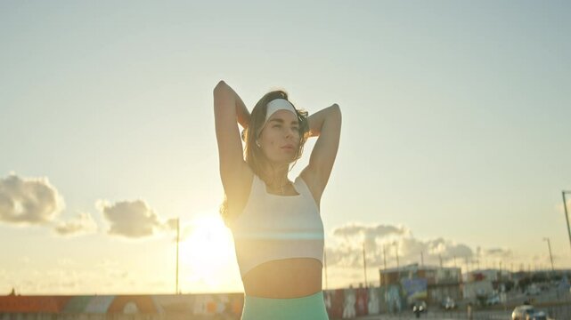 Sportswoman lifting dumbbell behind neck at sunset