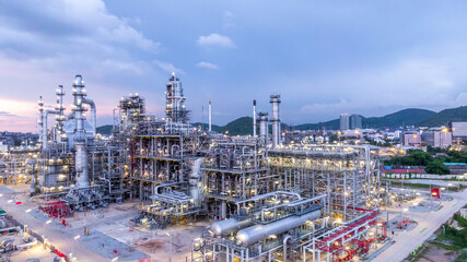 Obraz premium Oil refinery petrochemical plant at dusk illuminated storage tank industrial infrastructure, Oil refinery petrochemical product storage tank at oil refinery factory industry, Global energy refinery.