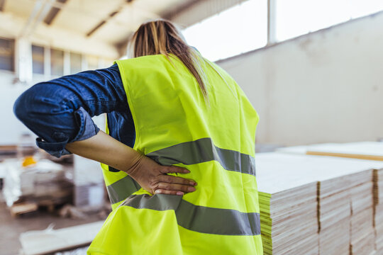Worker Experiencing Back Pain in a Construction Warehouse Environment