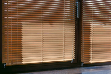 25mm wood venetian blinds cover large glass doors, casting subtle shadows in the sunlight. The warm tone and horizontal slats offer privacy and light control to the room. Sun protection.