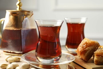 Tasty Turkish tea served with baklava and pistachios on wooden table, closeup