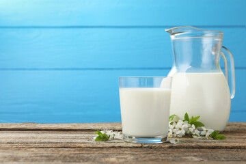 Fresh milk and blossoms on wooden table against light blue background. Space for text