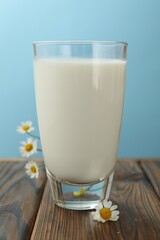 Fresh milk in glass and flowers on wooden table against light blue background, closeup