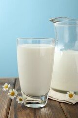 Fresh milk and flowers on wooden table against light blue background, closeup