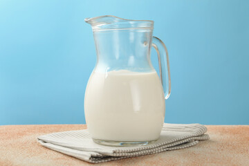 Fresh milk in jug on table against light blue background, closeup