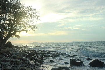 Golden hour on the coast. Warm sunlight bathes the rocky shore and calm sea. Captures a peaceful...