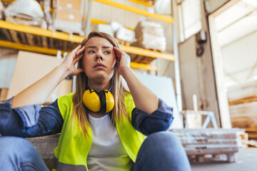 Stressed Female Worker in Warehouse Wearing High-Visibility Vest and Ear Protection