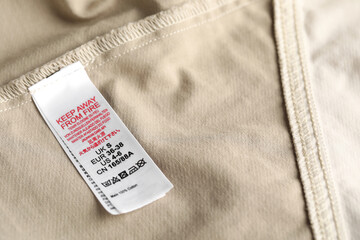 Obraz premium Clothing label with care symbols and size on beige garment as background, closeup