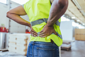 Worker in Safety Vest Experiencing Back Pain in Industrial Environment