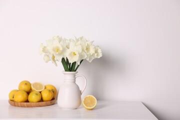 Beautiful daffodils in vase and lemons on white wooden table. Space for text