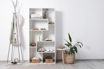 Fototapeta premium Shelving unit with different footwear, accessories, clothes and houseplant indoors. Shoe storage