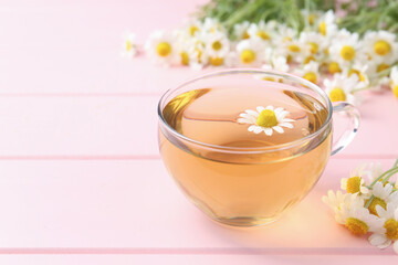 Delicious chamomile tea in glass cup and fresh flowers on pink wooden table, closeup. Space for text