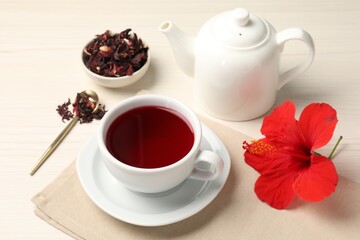Delicious hibiscus tea in cup, teapot, dry roselle sepals and flower on light wooden table