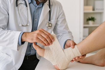 Doctor applying bandage to injured ankle of patient in clinic  