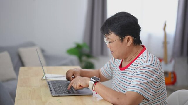 Focused individual working on a laptop at home, wearing glasses and casual clothing, surrounded by modern decor and warm lighting environment
