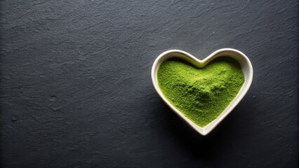 Obraz premium A heart-shaped bowl filled with vibrant green powder sits on a dark surface, a symbol of healthy living and natural goodness