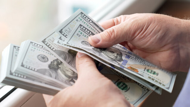 Male hands handling a large amount of dollars. Hundred-dollar banknotes in a person's hands. Financial transactions with cash money. Hands counting a stack of hundred-dollar bills.