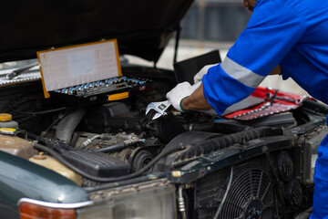 Auto mechanic repairing engine using wrench in garage. Mechanic in a jumpsuit fixes a car engine in...