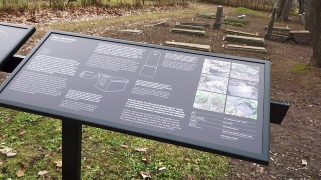 Informational sign titled &ldquo;Grave markers&rdquo; explains Jewish tombstone types and restoration efforts, set in a cemetery with visible graves behind it.
