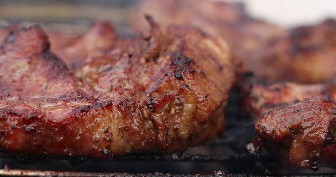 Beef steak on fire coals on iron grill in flame of smoke. Barbecue pork steak meat on grill. Roasting beef steak in burning charcoals fire on bbq grill. Beef steak grilling. Barbecue meat grill.
