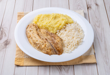 Grilled tilapia or saint peter with rice and mashed potato over wooden table