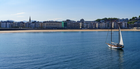 Obraz premium In the beautiful city of Donostia, a sailboat sails the waters of the sea in front of the iconic La Concha beach.