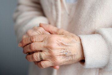 Fototapeta premium Close up captures senior adult's hands clasped together; a simple gold wedding ring on one finger. The skin shows wrinkles and visible veins