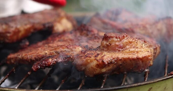 Beef steak on fire coals on iron grill in flame of smoke. Barbecue pork steak meat on grill. Roasting beef steak in burning charcoals fire on bbq grill. Beef steak grilling. Barbecue meat grill.
